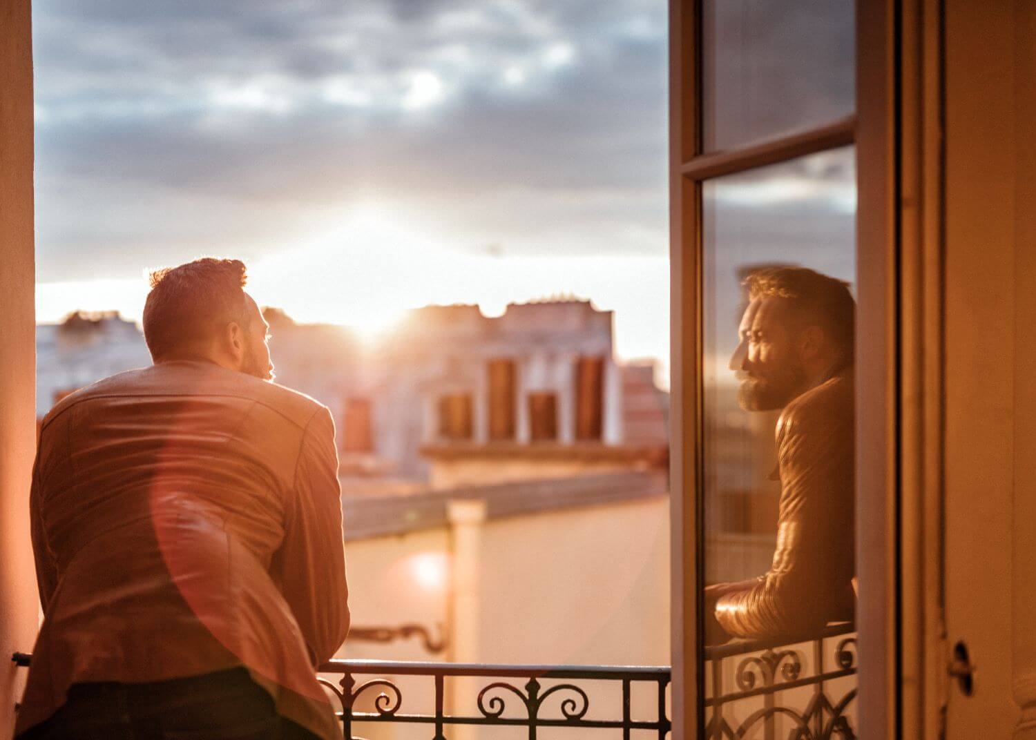 Man leaning on a balcony railing and looking over buildings at sunrise or sunset